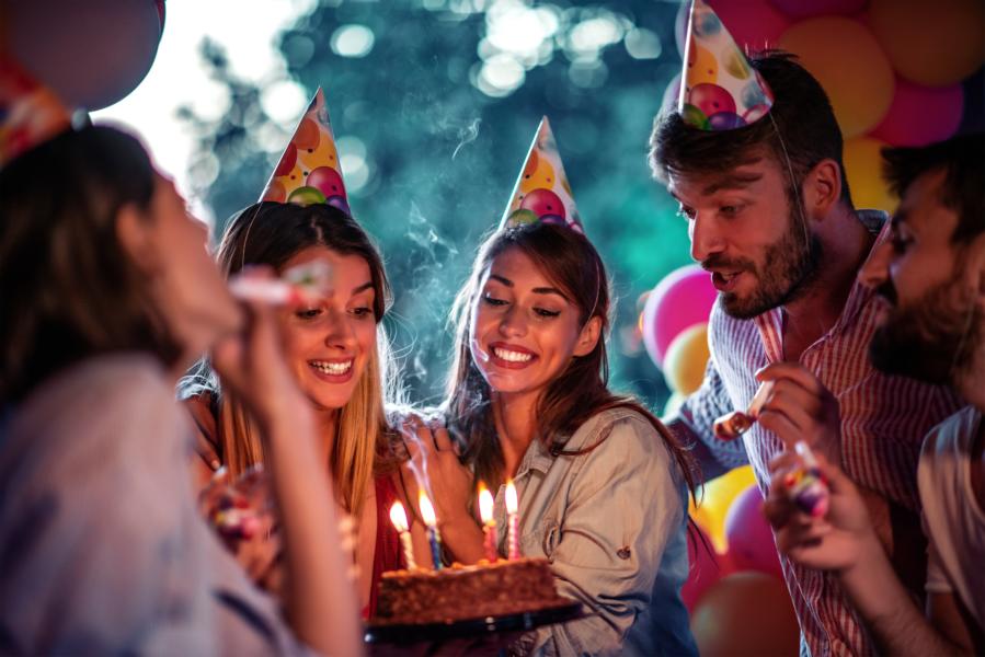 Freundesgruppe mit Partyhüten feiert Geburtstag mit Torte